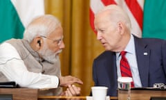 Narendra Modi and Joe Biden, behind a long table, turn to talk to each other