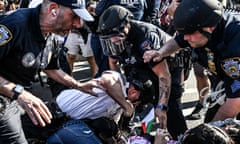 several police officers surround an officer who has his fist pulled back against a demonstrator lying on the ground