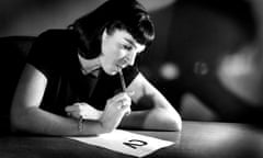 Black and white pic of woman sat at desk thinking with pen in mouth