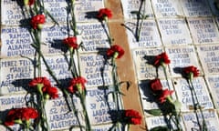 Red carnations left on small stone tablets with the names and ages of those killed