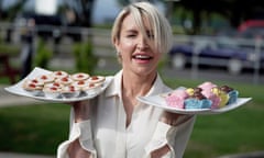 Heather Mills holding up plates of small cakes – cherry bakewells in her right hand, fondant fancies in her left, presumably vegan-friendly