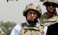 John Howard with a helmet and bulletproof vest on with military helicopters flying in the background