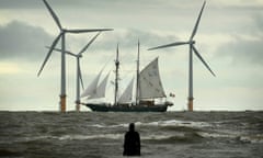 A sailing ship passes wind turbines and a figure from Antony Gormley’s Another Place near Liverpool.