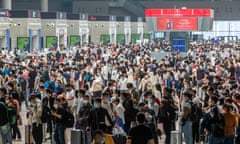 Crowds of people wearing masks and carrying luggage at a train station