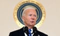 A man wearing a black suit and blue tie speaks at a lectern