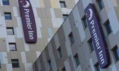 A modern-looking  Premier Inn hotel in London. There are two vertical signs with purple branding on cladding in varying shades of grey