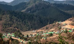 A settlement with green tarpaulins roofing bamboo huts and houses stretched along a valley