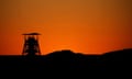 orange glow of the sky at dawn with the distinctly shaped pit head structure in silhouette