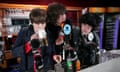 James Righton drinking from a tall mug of beer next to Jamie Reynolds with his mouth on a beer bottle and Simon Taylor-Davis of Klaxons at a bar