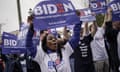 A Black woman with long hair wears a Biden T-shirt and holds a Biden sign among crowds doing the same.