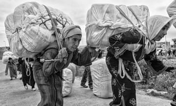 Two elderly women walk toward the Melilla crossing point carrying on their backs heavy bales of merchandise.