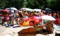 People sit and stand under umbrellas in the heat