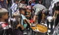 Palestinian children gather around a man ladling out food from a large container