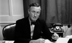 A black and white photograph of Ian Fleming sitting at his desk.