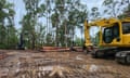 An excavator in a clearing with felled logs at the side