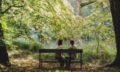 Two women sit on a bench looking out at a beautiful forest.