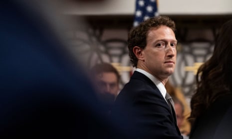 A boyish-looking white man with curly hair wearing a black suit, looks over his left shoulder seemingly at the camera, with what is likely someone's shoulder blurry in the foreground - a striking image.