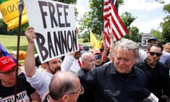 Clutch of people, entirely middle-aged white men, seen from above, all focused on one man dressed in all black, who has his arm around someone speaking to him, with someone holding a Free Bannon sign behind them.