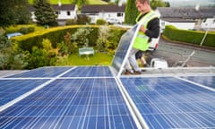 Workers installing solar electric panels on a house roof in Ambleside, UK