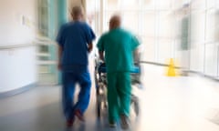 Doctor and a surgeon push a patient on a hospital bed trolley through accident and emergency department of a UK hospital.<br>H7XH3R Doctor and a surgeon push a patient on a hospital bed trolley through accident and emergency department of a UK hospital.