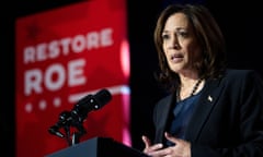Black woman, shoulder-length hair, black suit, speaking into microphone on stage in front of red sign that says Restore Roe.