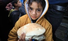 A Palestinian girl in a yellow coat holds flat breads