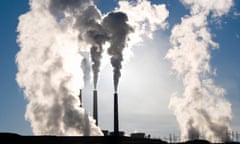 Photo of two smokestacks releasing puffy white clouds of steam into a blue sunny sky.