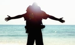 Man looking at sea, wearing a backpack, arms stretched out