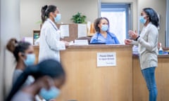 A female doctor and a female nurse are talking with a patient at the reception desk. They are all wearing face masks