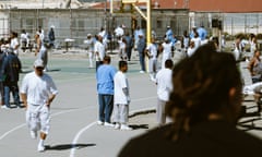 Dozens of men in white and blue T-shirts stand and play on a basketball court.