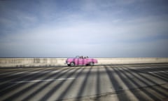 Flagposts installed outside the U.S. embassy cast their shadows on a vintage car with tourists on a sightseeing tour through Havana, December 18, 2015.  REUTERS/Alexandre Meneghini