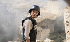 Léa Seydoux in a helmet and bullet proof vest with the word press on it, standing in bombed out ruins