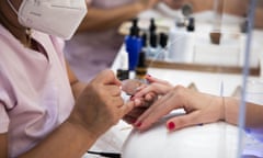 A close up of a manicurist in a nail salon painting a customer's fingernails with red polish.