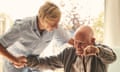 Smiling senior man with female healthcare worker. Home carer supporting old man to stand up from the chair at care home.