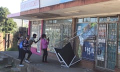 People take pictures of a damaged shop in Mbabane, Eswatini, following protests.