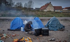 A refugee sits by a fire to keep warm at a camp on the outskirts of Calais.