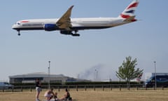 People enjoy the hot weather in a field beneath a British Airways flight coming into land at Heathrow airport, London on 19 July 2022