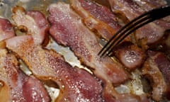 Closeup of a fork prodding bacon frying in a pan