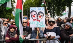 A crowd of people on a pro-Palestine march stand behind barriers and hold flags and banners