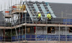 Builders stand on scaffolding as they work on the roof of a house on a housing development