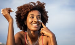 A beautiful cheerful black woman is applying sunscreen on her face, she is enjoying a vacation and a little luxury in her life.