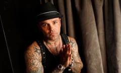 white man with tattoo sleeves wearing black fedora puts his hands together