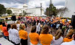 people, many wearing orange t shirts, gather outside grand building