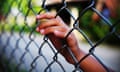 Teenager in jail or detention with hand grasping wire fence