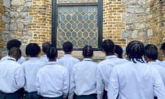 A row of Black schoolboys show off their hairstyles outside a school building