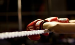 A pair of arms, red boxing gloves on the hands, hanging over the rope of a boxing ring