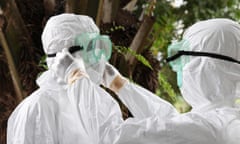 Liberian nurses put on protective clothing as preparation to carry the body of an Ebola victim