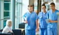 junior doctors<br>three junior doctors walking along a hospital corridor discussing case and wearing scrubs. A patient or visitor is sitting in the corridor as they walk past . Medical students hospital UK