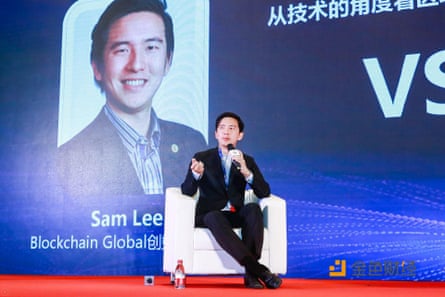 Sam Lee sitting in an armchair on a stage, speaking into a microphone 