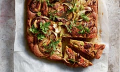 Topview of a focaccia-like flattened loaf of bread topped with slivers of zucchini, red onion and herbs.